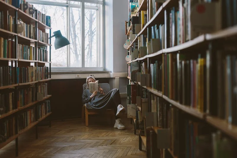 imagen de una estudiante sentada en una biblioteca mientras lee su libro